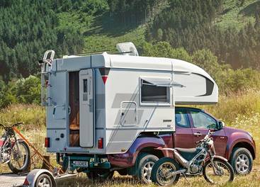 Tischer camper TRAIL/BOX 200 på en brunröd pickup med släp omringad av motorcyklar