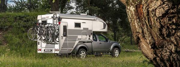 Tischer pickup camper TRAIL 260SD på en silverfärgad Nissan Navara med omtypning och höjda vikter stående i en skog 